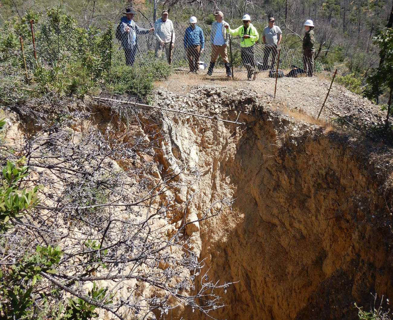 photo of a group of 7 people standing outside of a fenced off mine shaft.