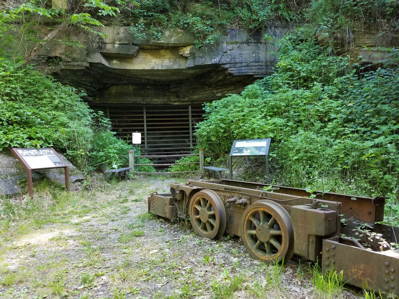 a gated mine opening with a display of old machinery and interpretive signs