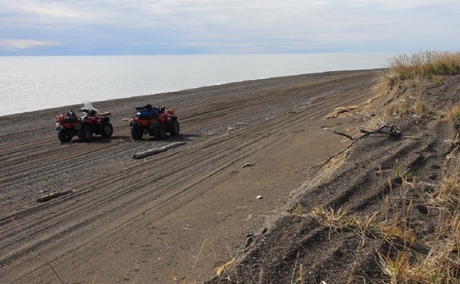 Two ATV's on an empty beach, grass in the foreground.