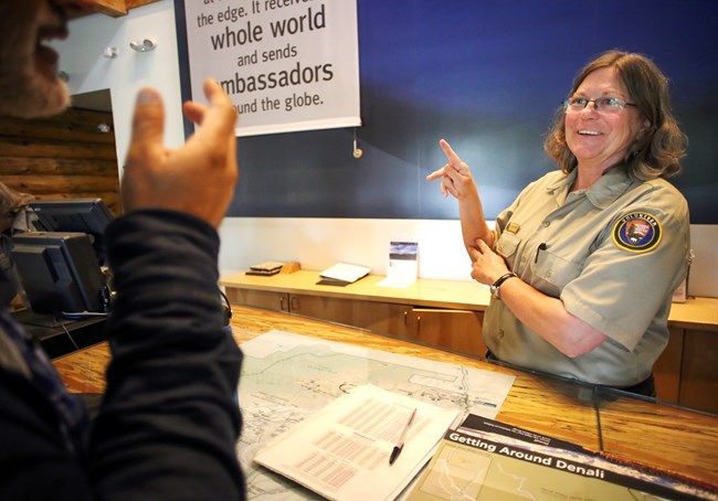 Female Denali NPS Ranger in uniform signing to a visitor