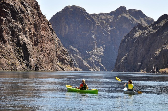 2 kayakers on water surrounded by distant cliffs