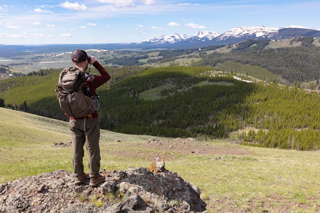 Yellowstone Man in hiking attire looking at distant mountains with binoculars