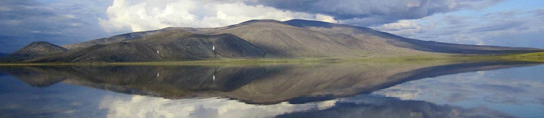 Low rolling mountains and clouds reflected in water at Noatak National Preserve.