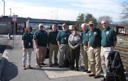 A group of volunteers and a ranger await the train near a train station. A group of volunteers and a ranger await the train near a train station.