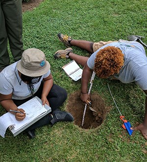 Two people measure the depth of a hole and record information on a clipboard. NPS photo.