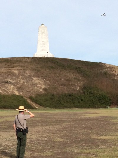 A man in a hat stands in a field saluting towards a large monument