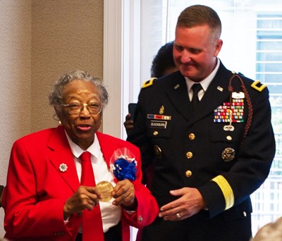 Jones Cong. Gold medal An older lady in a red coat holds up a gold medal while standing next to a man in a dark blue coat