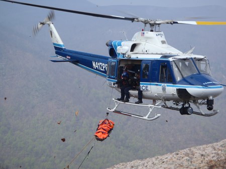 A helicopter hovers while an orange basket is pulled into the helicopter
