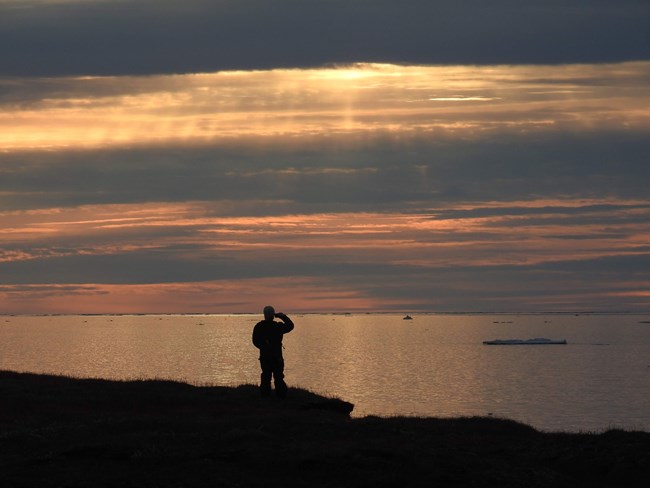 a man stands on ocean shore at dusk