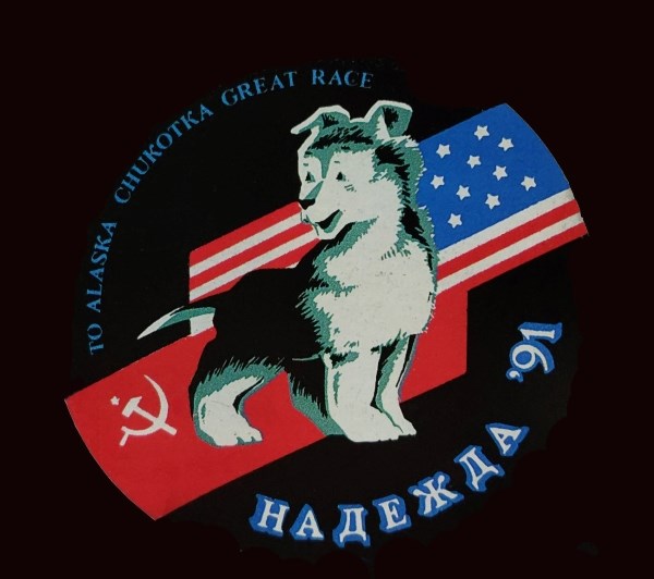 An illustration of a race dog in front of the Soviet Union and American flags with text that reads “To Alaska Chukotka Great Race” followed by “Надежда ‘91.”