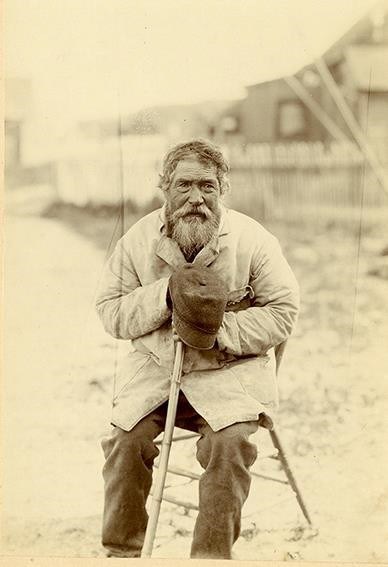 an old man sitting on a chair, village street on the background