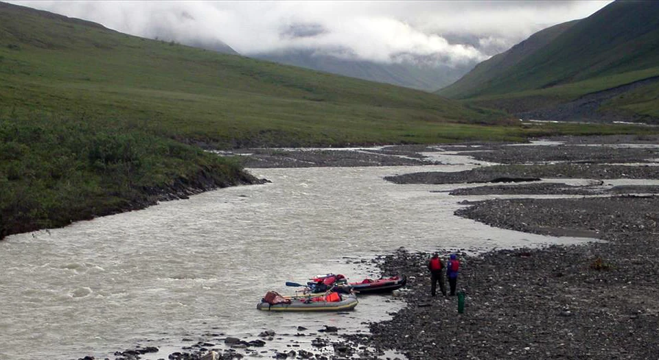 researchers on the river resized two people with inflatable kayaks on the bank of a river with mountains in the background