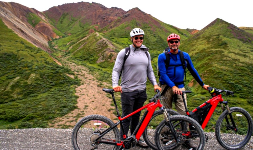 Two men pose with red bikes on treeless mountain trail