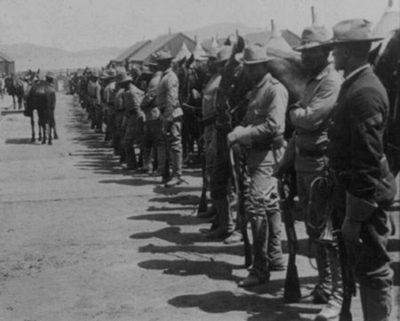 Several African American soldiers stand at the ready in front of their horses