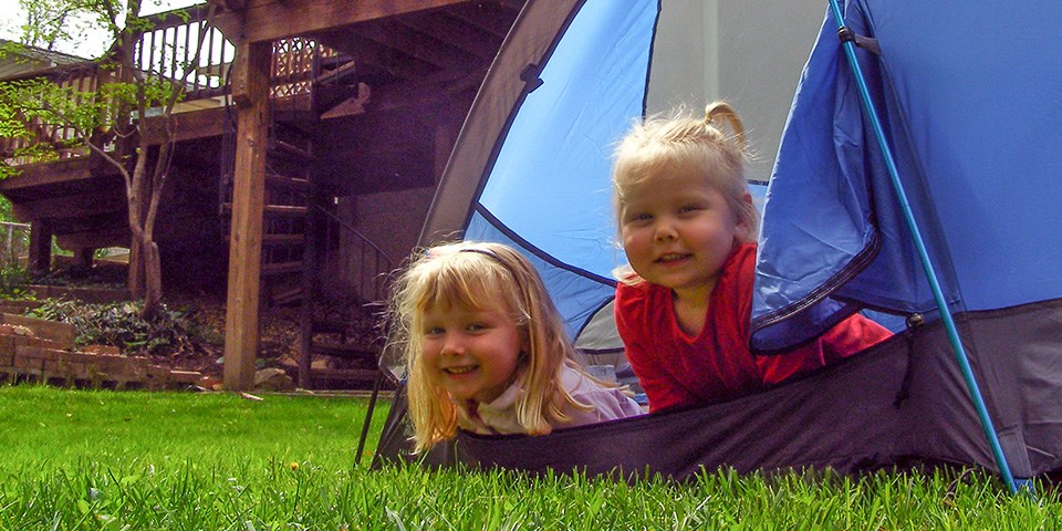 Two children peeking out of their tent in the backyard