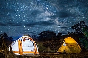 Two tents are illuminated from the inside with stars shining above