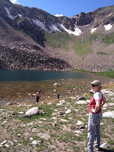 KristyBcampinglake woman standing at the edge of a lake surrounded by mountains