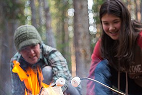 A woman and a youth roast marshmallows over a campfire