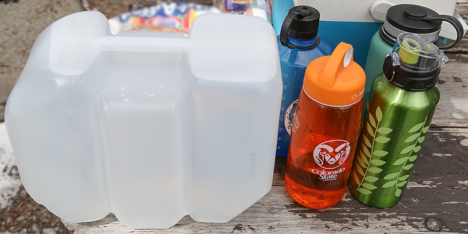 A jug of water and four water bottles sit on a picnic table