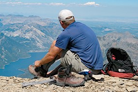 A man sits on a mountain top overlooking a lake