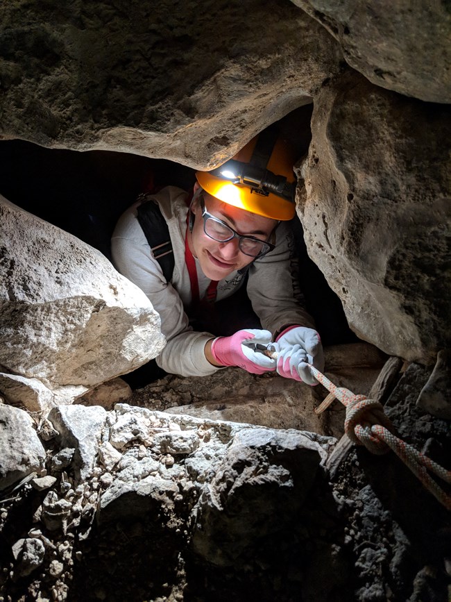 photo of a person exploring a small cave opening.
