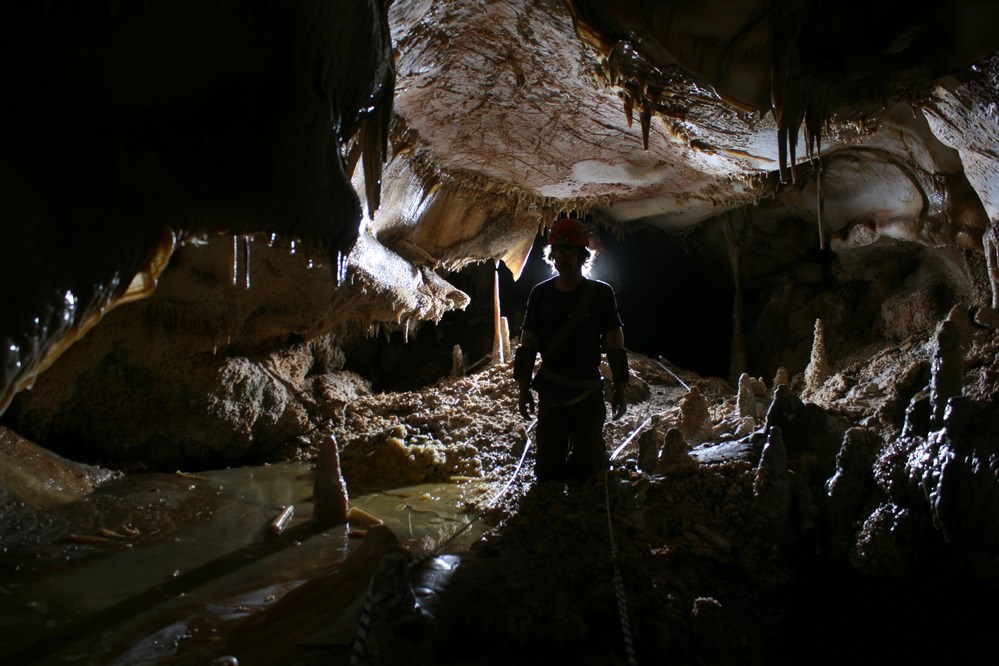 caver in wet area of cave with stalactites and stalagmites