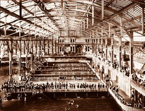 historic photo taken inside of a large arch-roofed building over a swimming pool
