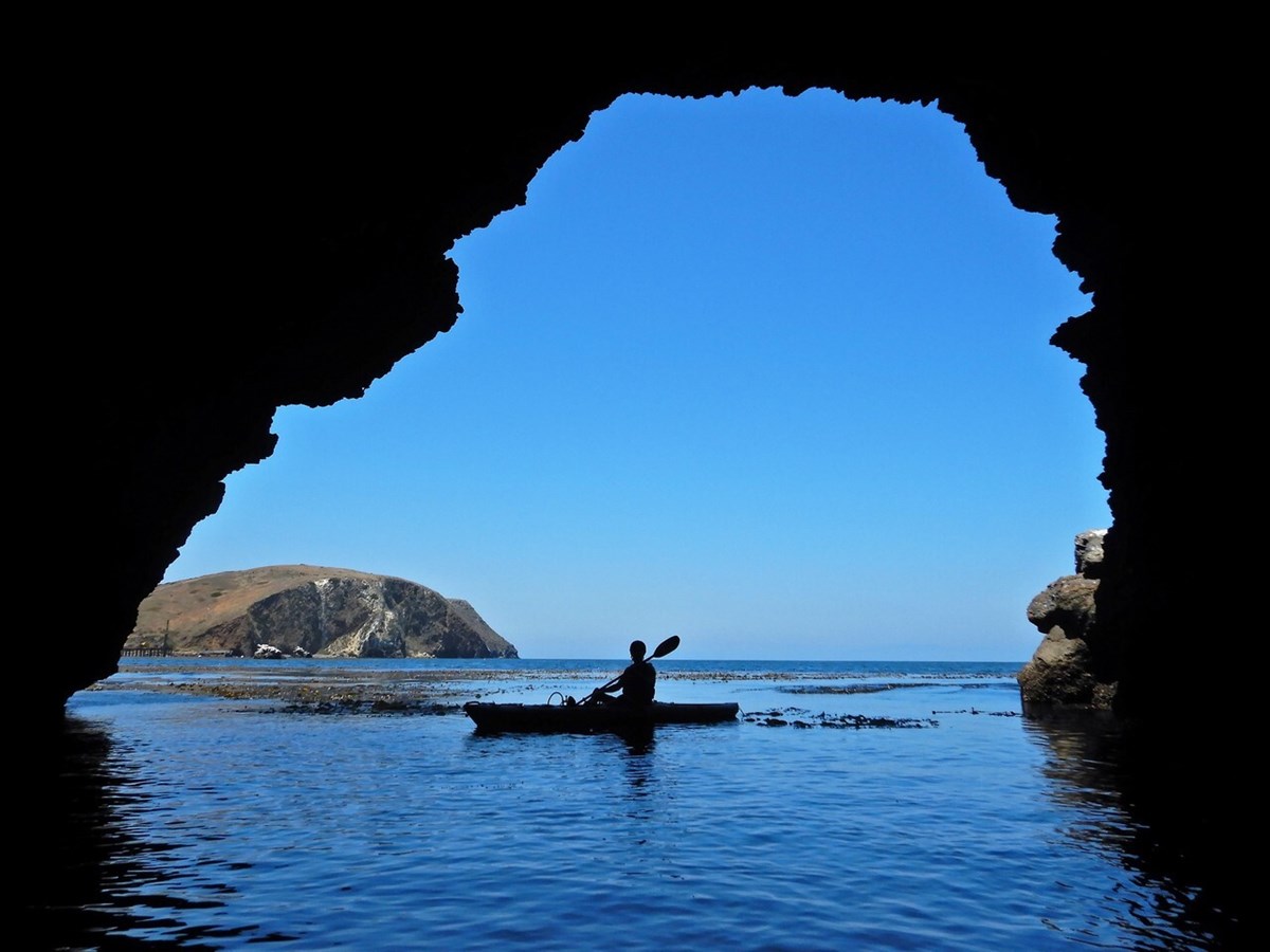sea kayaker paddles past a cave opening