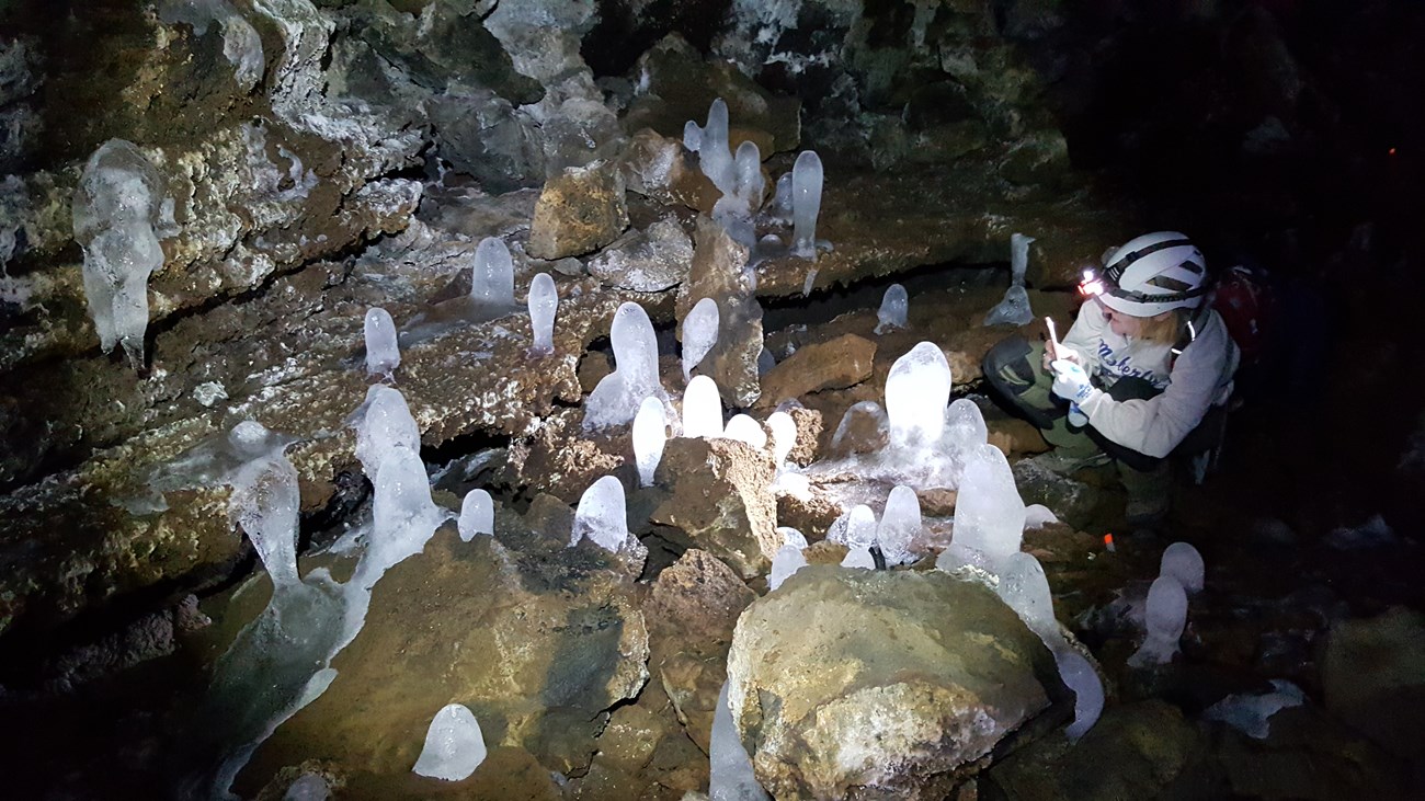 a person wearing a climbing helmet in a cave with several small ice formations