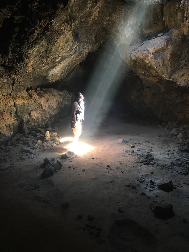 a person standing in a shaft of light in a lava tube