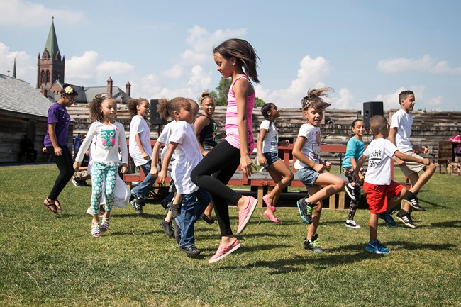 children dancing in grassy area with historic buildings in the background