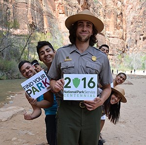 Zion Centennial Launch -- text box square rangers and young people holding centennial logo signs in small canyon