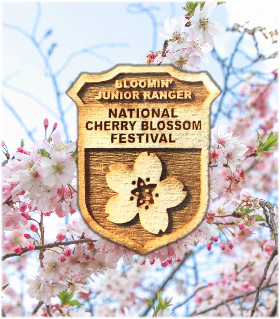 Bloomin' Junior Ranger Badge A wooden junior ranger badge with a carved cherry blossom sits atop a background of cherry blossoms