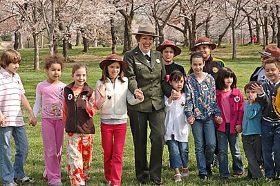 Kids with a park ranger at the National Cherry Blossom Festival standing outsider under blooming cherry trees