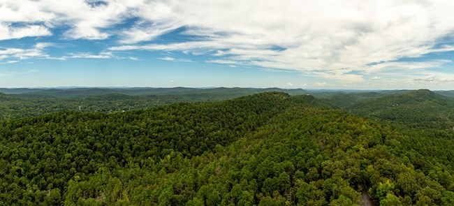 Rolling, forested hills stretch toward the blue sky horizon