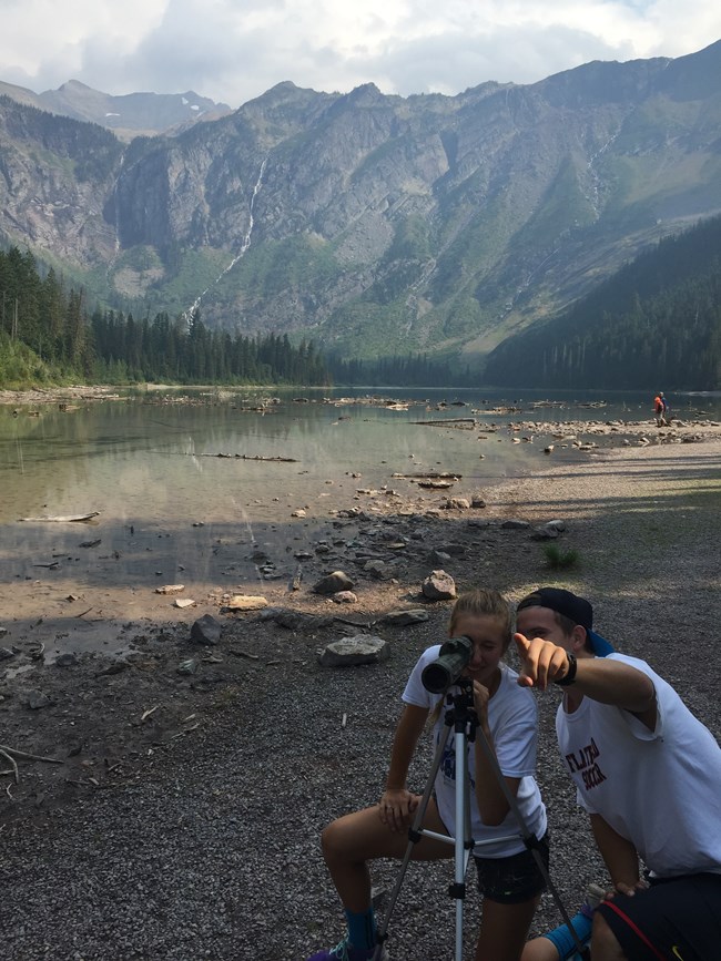 two people use a spotting scope in an alpine lake setting two people use a spotting scope in an alpine lake setting