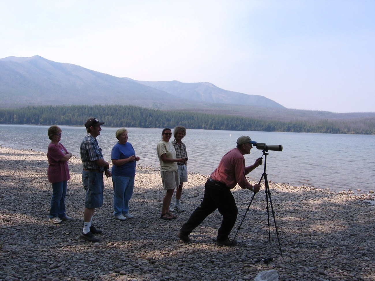 Six people gather on a rocky beach with a spotting scope.