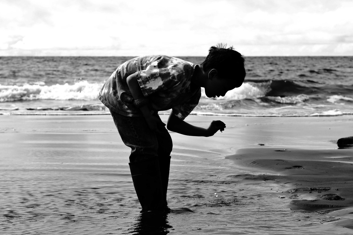 black and white silhouette of a child picking something out of the ocean