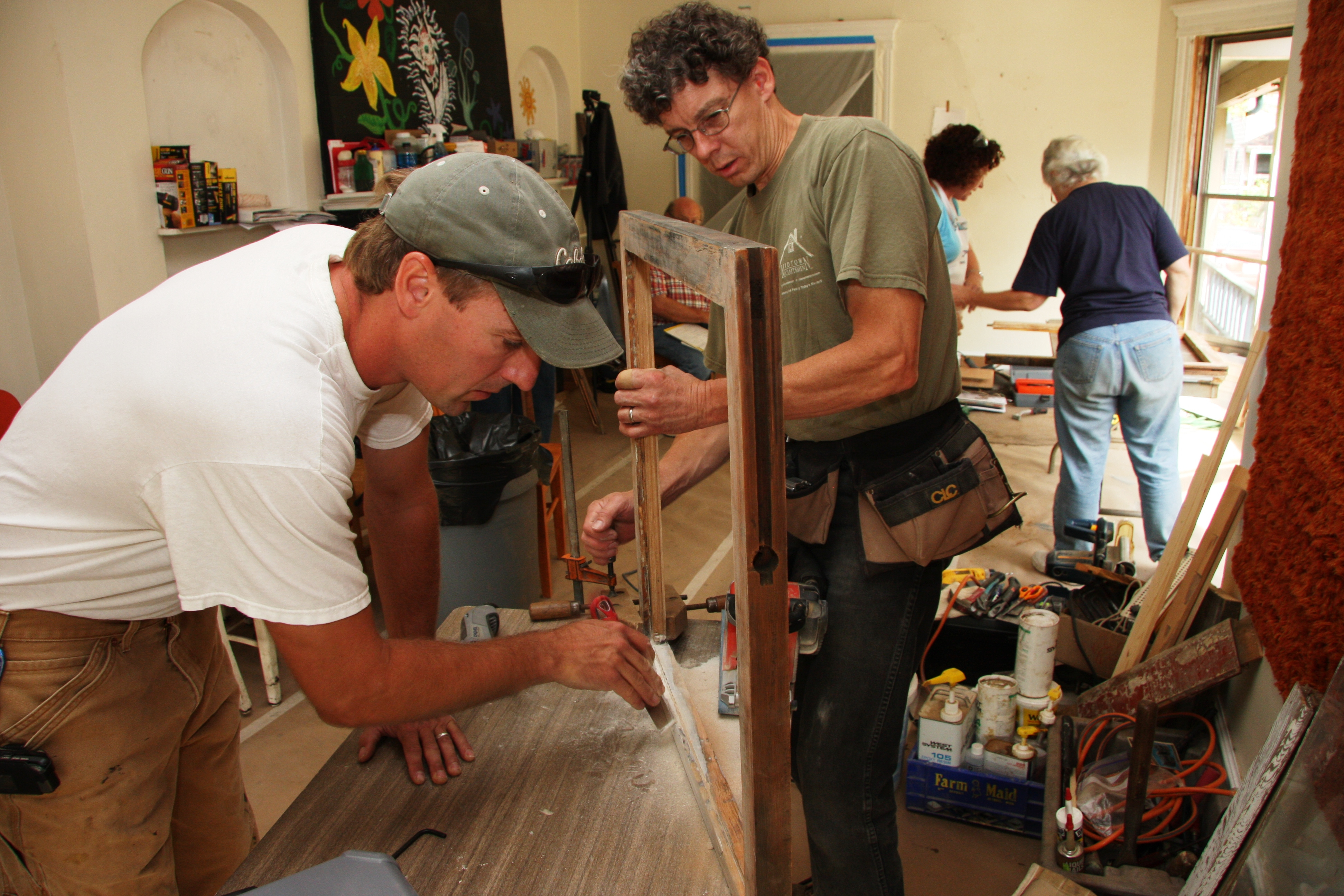 Two people look at a wooden window sash