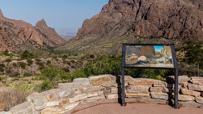 An NPS sign on a cliff overlooking deep, rocky valleys.