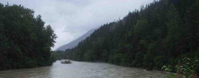 The Taiya River with dark clouds hanging heavily above it and dense forest looming on either shore.