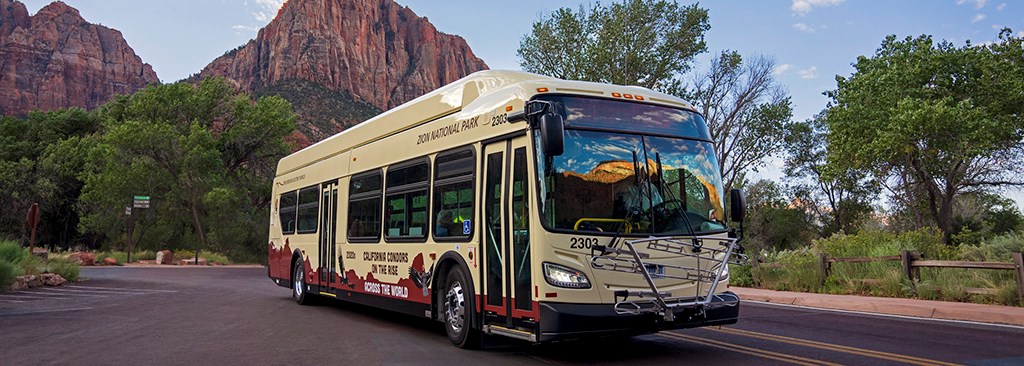 Zion Shuttle Bus A large, new bus in the foreground with sandstone peaks in the background