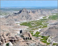 Aerial view looking at grassy valley surrounded by reddish-brown badland formations