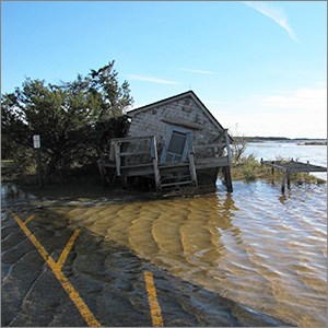 A white shack it leaning dangerously into water lapping over pavement