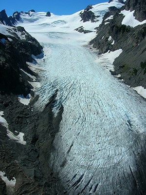 White glacier spilling downhill with blue sky and mountains in background