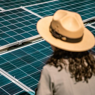 An array of solar panels sits atop the roof of a park building with a uniformed ranger in the foreground