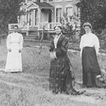 Clara Barton at Glen Echo house, historic Three women in long dresses stand in a yard near a house