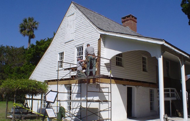 Work on Kitchen House at Timucuan Ecological and Historic Preserve Two NPS staff on scaffolding to work on the second floor exterior of a wooden structure.