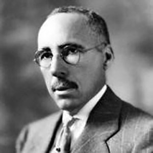 Portrait of David Williston: Slender African American man with short hair, mustache, glasses in a suit and tie.