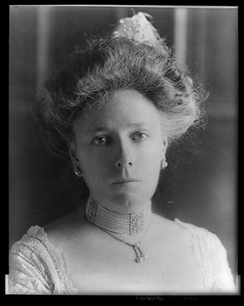 Portrait of woman with hair pulled away from her face, earrings and necklace, and straight-faced expression